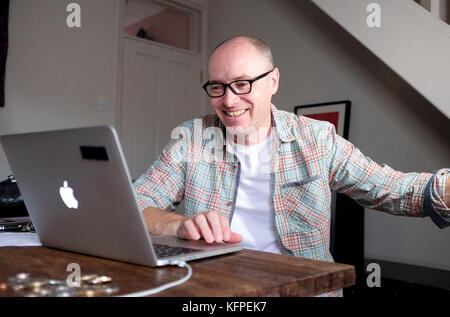 Mature middle aged man smiling using an Apple Macbook Pro laptop computer Stock Photo