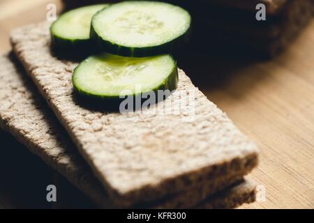 Bread made from rye and wheat flour with freshly sliced and green pieces of cucumber, lie on a board for cutting food. Prepared for making delicious s Stock Photo