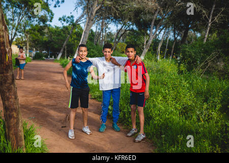 Three kids posing for a picture with their dirty shoes after playing a soccer game in the woods , Harhoura, Morocco Stock Photo
