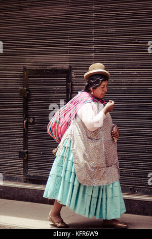 A woman is seen walking on the streets of La Paz, wearing the traditional clothes and the peculiar hat. La Paz,Bolivia Stock Photo