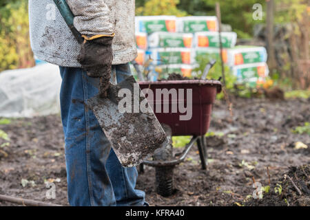 Gardener holding a spade after removing old weed membrane and wood bark from a vegetable garden made up of wet heavy soil. Scottish borders, Scotland Stock Photo