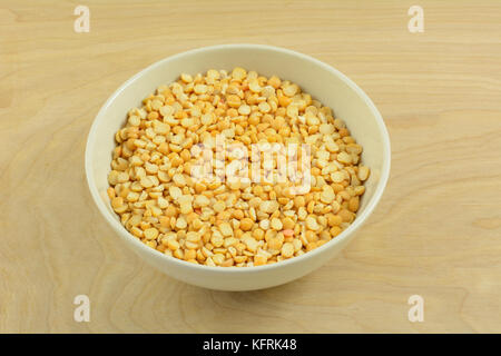 Dry raw yellow split peas in white bowl on wooden table Stock Photo