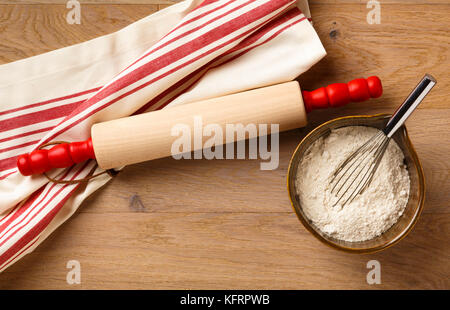 Kitchen table counter countertop with cooking utensils wooden rolling pin and cotton dish towel dishtowel, and baking ingredients white flour in bowl Stock Photo