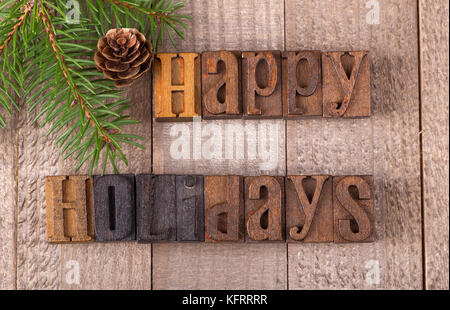 Happy holidays text on a wooden surface with evergreen tree branch and pinecone Stock Photo