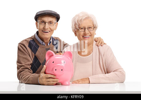Senior couple with a piggybank seated at a table looking at the camera and smiling isolated on white background Stock Photo