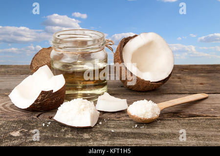 Halfs of coconut, jar of coconut oil, coconut flakes on blue cloudy sky background. Healthy food concept Stock Photo