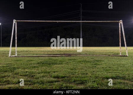 Empty soccer practice field at night looking through a goal without a net down the field to the other goal with the green grass lit up by the lights a Stock Photo