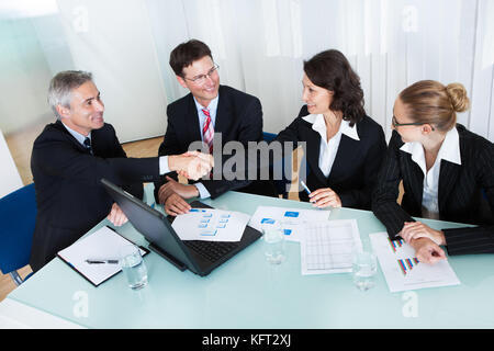 Busines colleagues seated around a table in a meeting congratulating one another by shaking hands Stock Photo