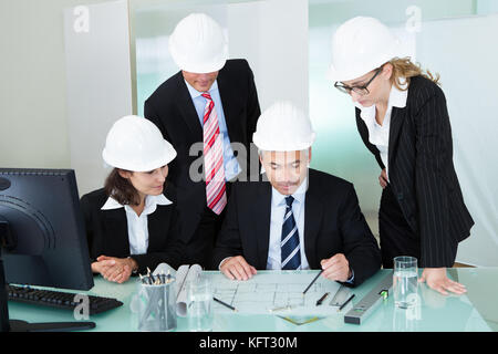 Meeting of four diverse architects or structural engineers in hardhats and suits seated in an office Stock Photo