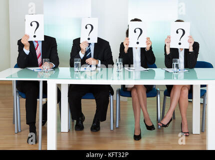 Row of businesspeople with question marks signs in front of their faces Stock Photo
