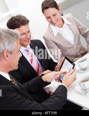 Business colleagues enjoying a coffee break smiling at something on the screen of a tablet held by one of the men Stock Photo