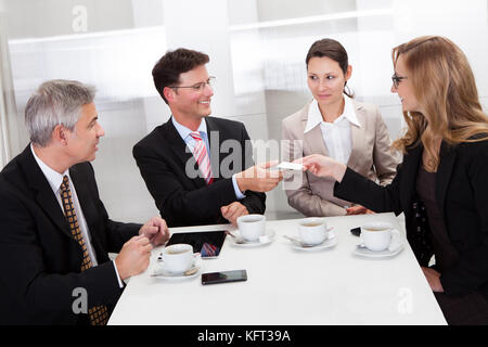 Businesspeople exchanging cards over coffee while having an informal meeting in a cafe Stock Photo
