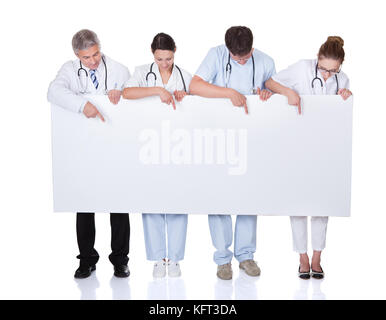Four attractive professional diverse medical staff holding up a long horizontal blank white banner for your text or advertisement Stock Photo
