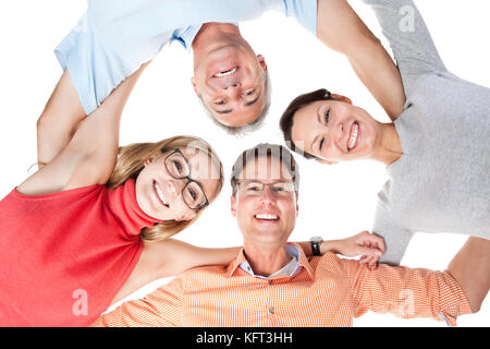 Low angle view of a group of happy middle aged friends with joyful smiles standing arm in arm looking down at the camera Stock Photo
