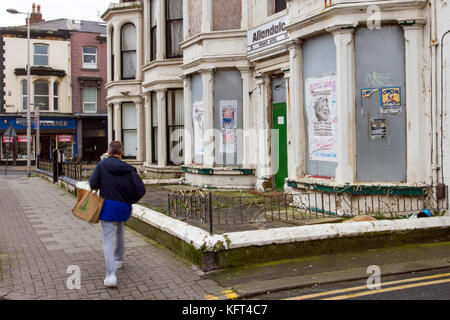 Residential boarded up houses. Figures passing Retail units To Let, Closed, Closing down, Shuttered shops, businesses in decline, with poor retail sales.   The Malaise affects British Seaside resorts. Blackpool, Lancashire, UK Stock Photo