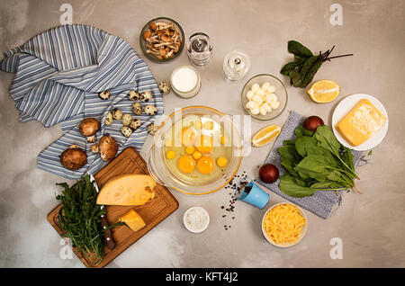 Overhead of ingredients frittata quishe vegeterian diet meal. Eggs in bowl, quail eggs, milk, cheese mozzarella, gouda, tomato, spinach, mushrooms, ch Stock Photo