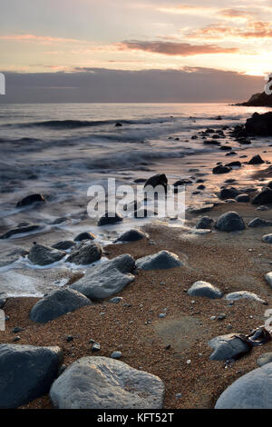 A beautiful and atmospheric seascape with wet rocks in the foreground and sandy beach with waves breaking on the shoreline at sunset. Atmosphere. Stock Photo