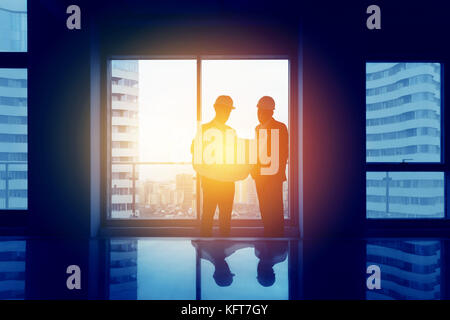 Silhouettes of two engineers with big blueprint in hands are discussing something. Engineering concept Stock Photo