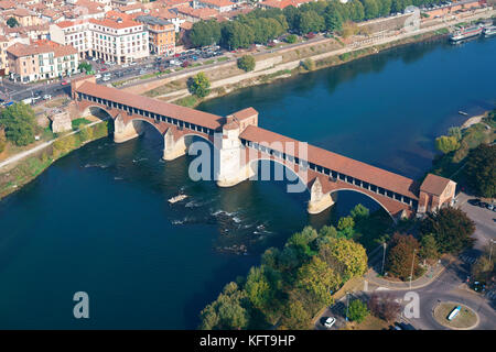 AERIAL VIEW. Historic covered bridge (Ponte Coperto) across the Ticino River, a small chapel stands at the middle. Pavia, Lombardy, Italy. Stock Photo