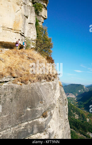 AERIAL VIEW. Two young women hiking on a trail 'in the sky' below the watchful eye of the sandstone guardian. Annot, Alpes-de-Haute-Provence, France. Stock Photo