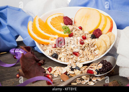 Healthy breakfast. Muesli with orange fruit, apple, pomegranate, nuts, banana and honey in white bowl over on old wooden table. Healthy organic natura Stock Photo