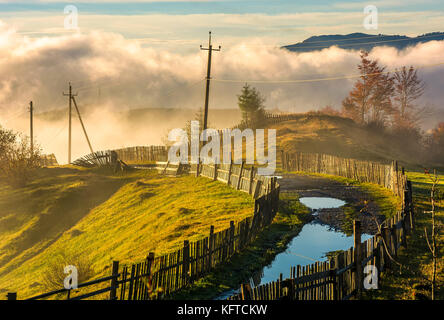 rural road among the wooden fences in morning fog. spectacular scenery in mountains at sunrise Stock Photo