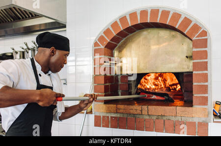 Chef baking pizza in the wood fired oven at commercial kitchen. Cook baking pizza in a traditional stone oven at restaurant. Stock Photo