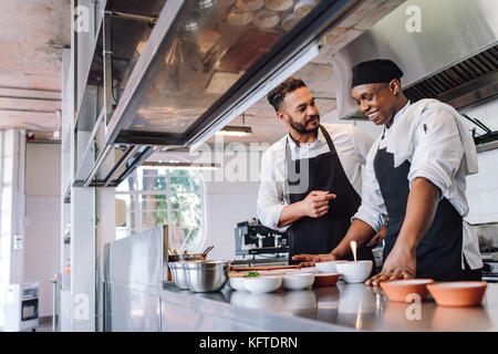 Happy men chefs cooking food at cafe kitchen. Two cooks making food dishes in restaurant kitchen. Stock Photo