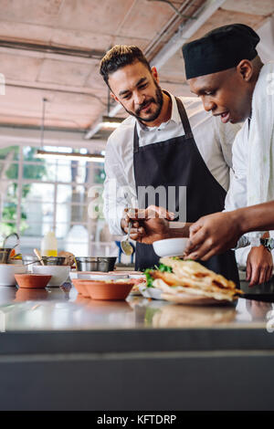 Two professional chefs working in restaurant kitchen. Chefs cooking new food dish at commercial kitchen. Stock Photo