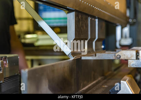 worker operating metal press machine at workshop. Stock Photo