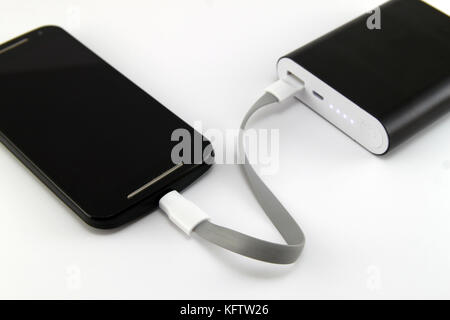 Smartphone charging from black power bank isolated on white background. Smartphone and power bank concept. Stock Photo