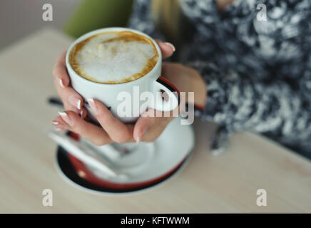 Cappuccino with thick foam in manicured hands of woman Stock Photo