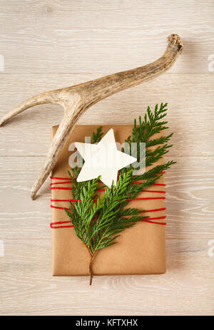 Christmas gift present wrapped in recycled kraft wrapping paper with natural antler and evergreen decorations and a blank, star-shape gift tag Stock Photo