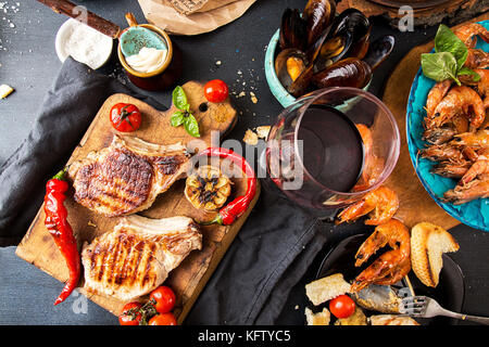 Overhead of dinner table. Assorted delicious grilled barbecue meat and seafood with vegetable. Pork grilled steaks, grilled baked mussels, shrimps, ch Stock Photo