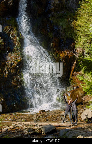 Couple of hikers posing in front of a beautiful waterfall Stock Photo