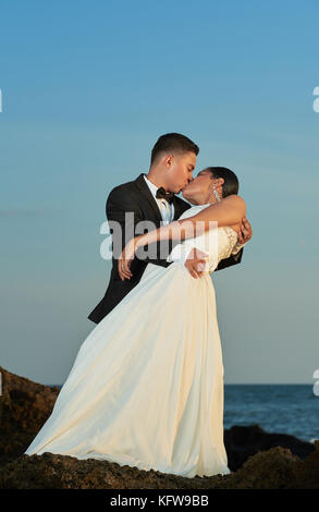 Groom kissing bride on blue sky background at ocean beach Stock Photo