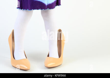 Little girl feet in high heel shoes. Close-up of child feet in mothers shoes on white background. Child has fun with mothers footwear. Funny kid backg Stock Photo