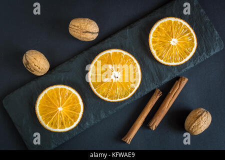 Dry slices of orange fruits, walnuts and cinnamon on a black slate background. Stock Photo