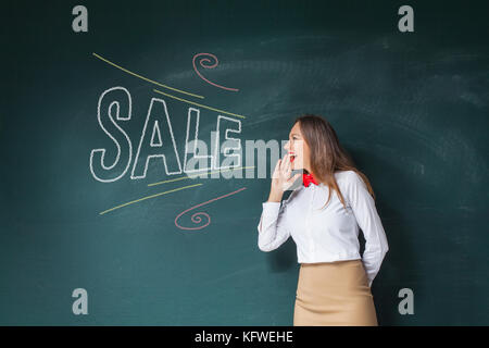 Young girl keeping hand near mouth and screaming, standing against blackboard Stock Photo