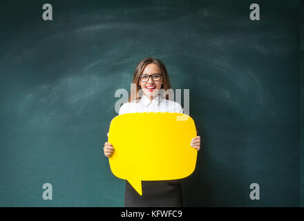 Young woman holding yellow speech bubble on blackboard Stock Photo