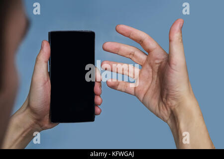 The guy looks at his phone with confusion. Talking on video chat on mobile. Blank for image. The black phone. Stock Photo