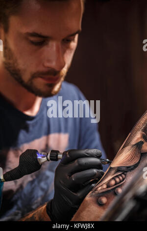 Professional tattoo artist makes a tattoo on a young man's hand Stock Photo