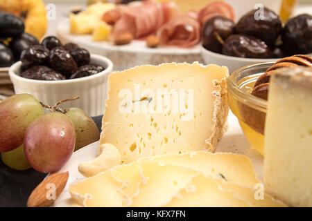 Slices and blocks of cheese, prosciutto, olives, grapes, honey and figs on white wooden cutting board Stock Photo
