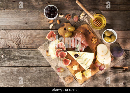 Food composition with cheese plate with cheese, dry meats, various fruits and nuts. Overhead of set of pieces moldy cheese, prosciutto, pickled plums, Stock Photo