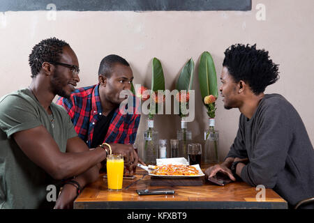 Three men eating nachos at a restaurant Stock Photo