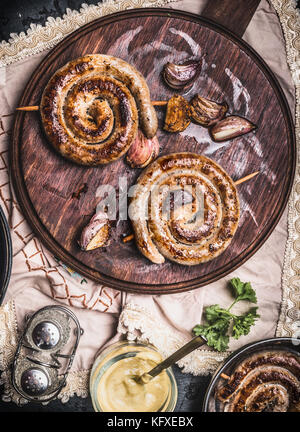 Grilled sausages spiral served on rustic round cutting board with mustard , top view, Country dark style Stock Photo