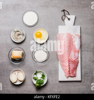 Various cooking ingredients for Fish patties in bowls: fish fillets , egg, shrimps , onion ,bread, flour on on gray stone background  , top view Stock Photo