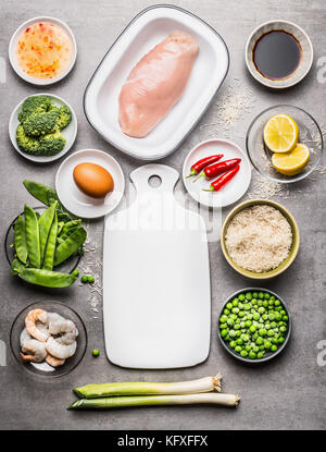 Fried rice cooking ingredients with chicken , egg , shrimps and green vegetables around white cutting board  on gray stone background  , top view Stock Photo