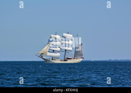 Square-rigged white sailing ship at sea with a distant shore in the far background Stock Photo
