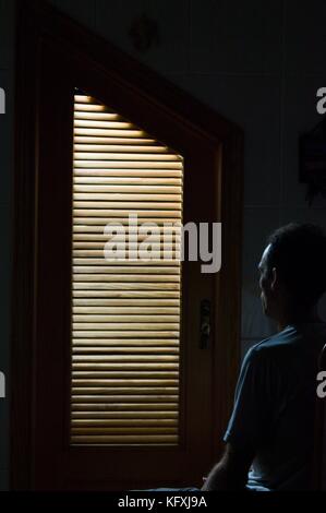 Door of cupboard with flushed light within illuminating a seated man looking at the door